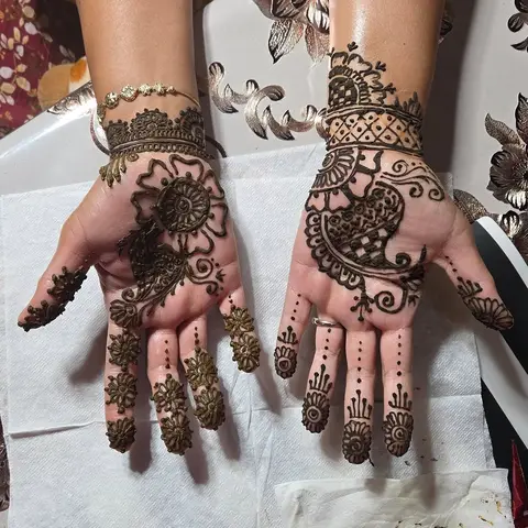 Two palms covered in dense traditional mehndi, with mandalas and finger bands